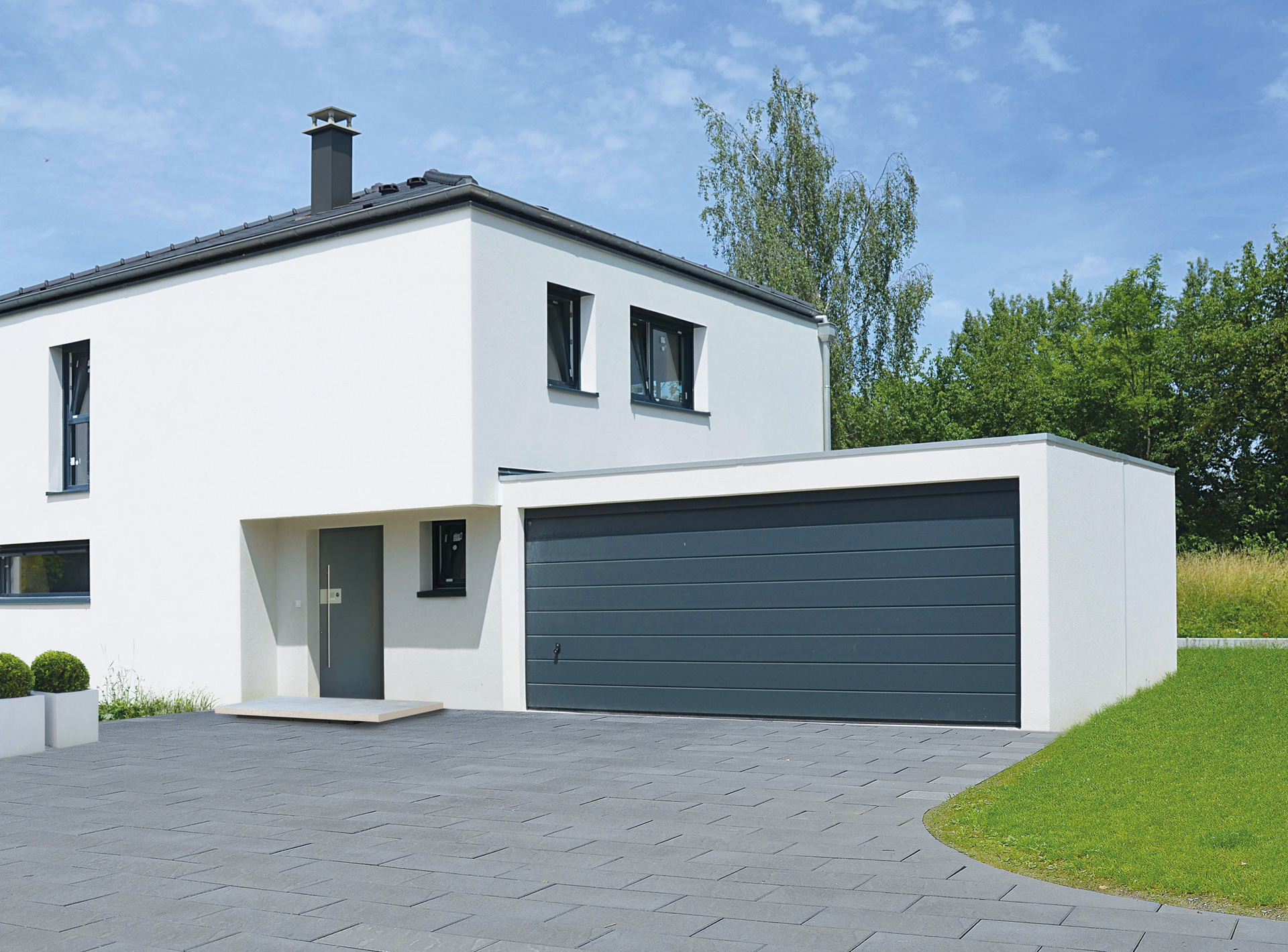 Modernes weißes Einfamilienhaus mit anthrazitfarbener Doppelgarage, grauen Fenstern und gepflasterter Einfahrt