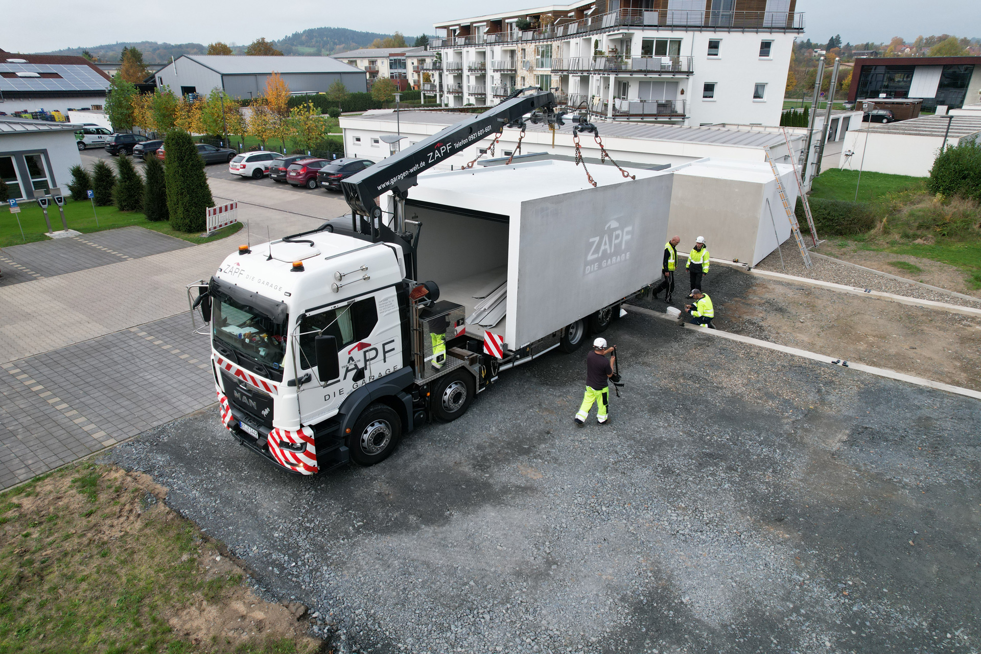 "ZAPF Spezial-LKW mit Kran bei der professionellen Fertiggaragen-Montage, vier Monteure in Sicherheitskleidung beim Aufbau