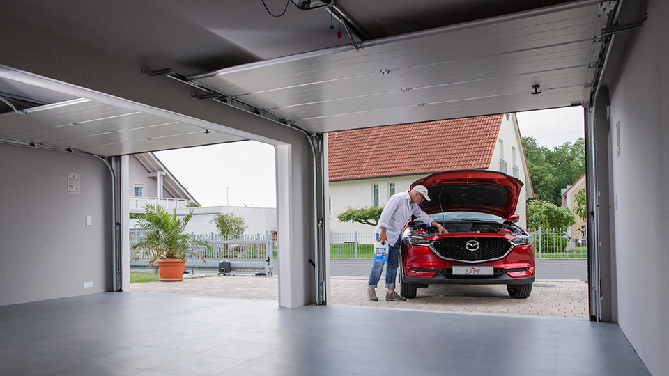 Innenansicht einer Betonfertiggarage mit offenem Tor – Mann reinigt rotes Auto vor moderner Garage von ZAPF