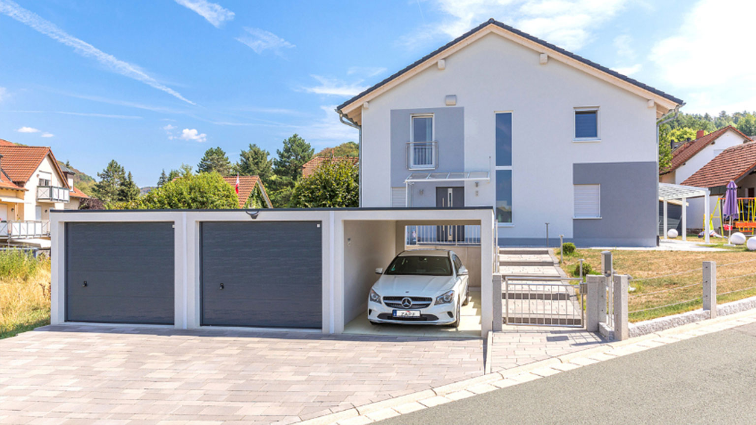 Moderne Dreifachgarage mit zwei geschlossenen Toren und einem offenen Stellplatz vor einem Einfamilienhaus.