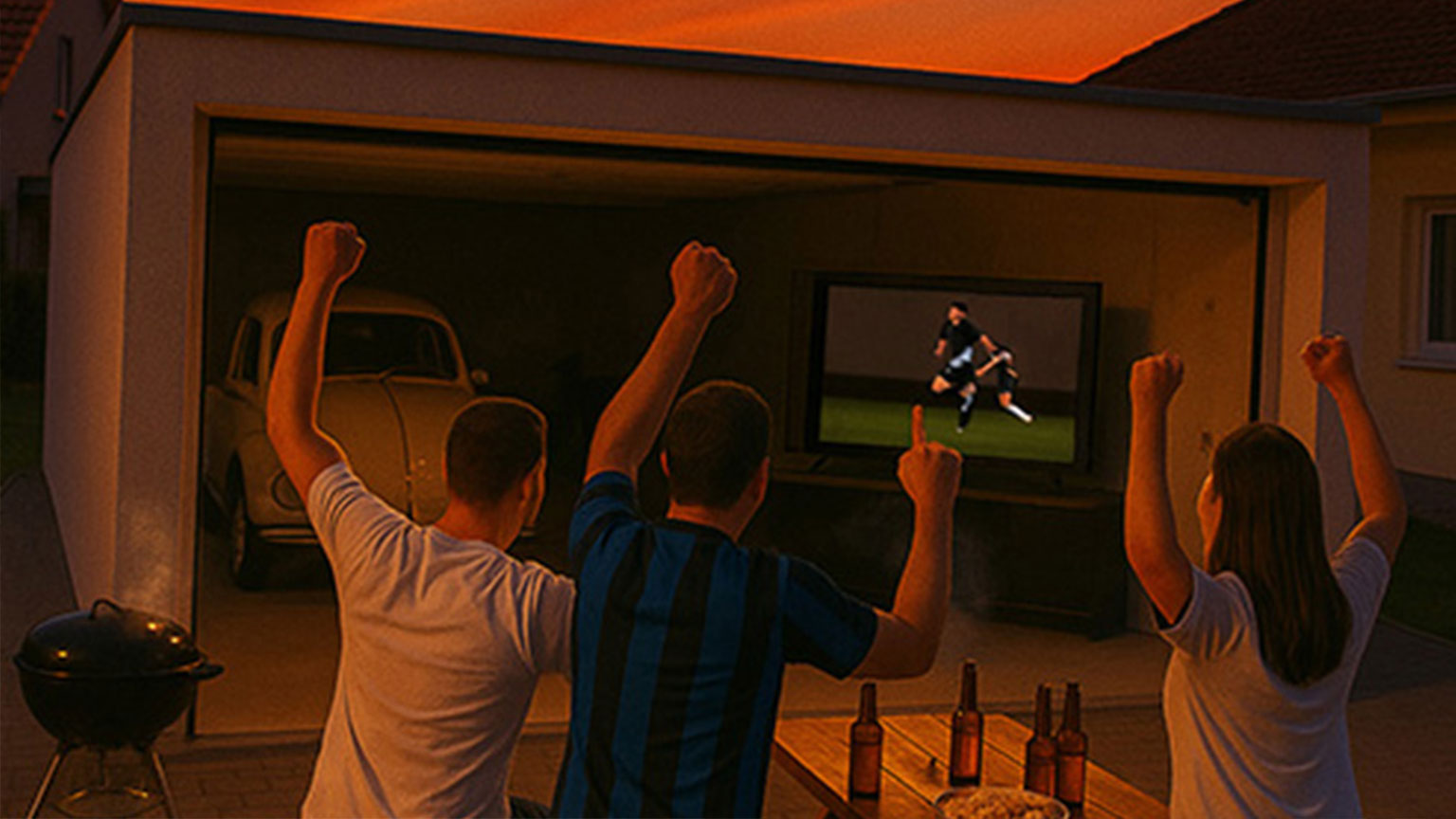 Drei Personen jubeln beim Fußballschauen vor einer offenen Garage mit Fernseher – geselliges Public Viewing bei Sonnenuntergang.