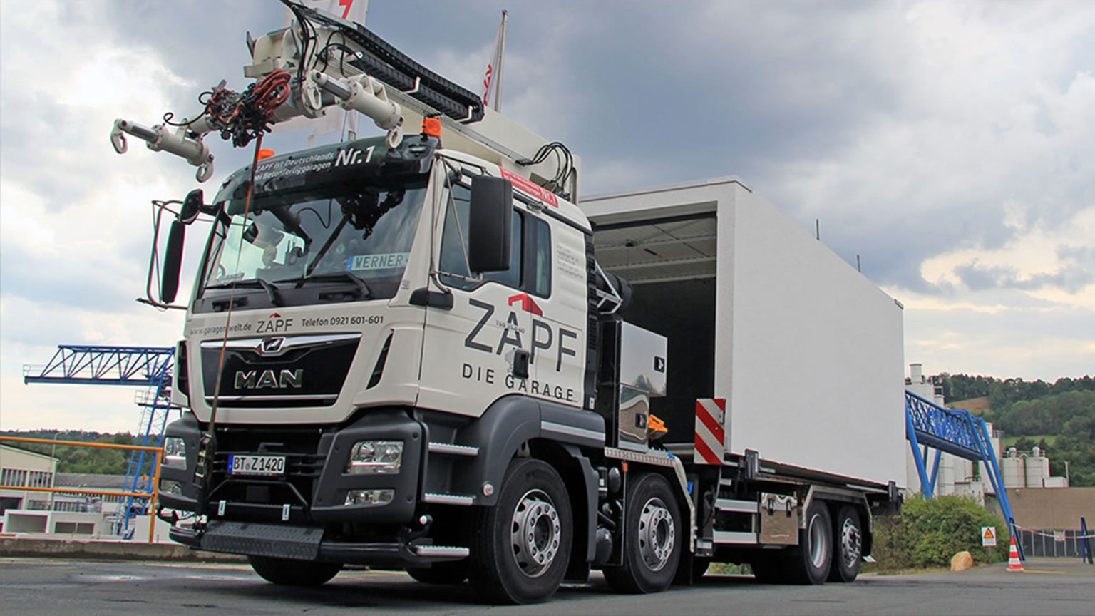 APF-LKW transportiert eine Fertiggarage auf einem Auflieger – moderner Schwerlasttransport vor Industriehintergrund.