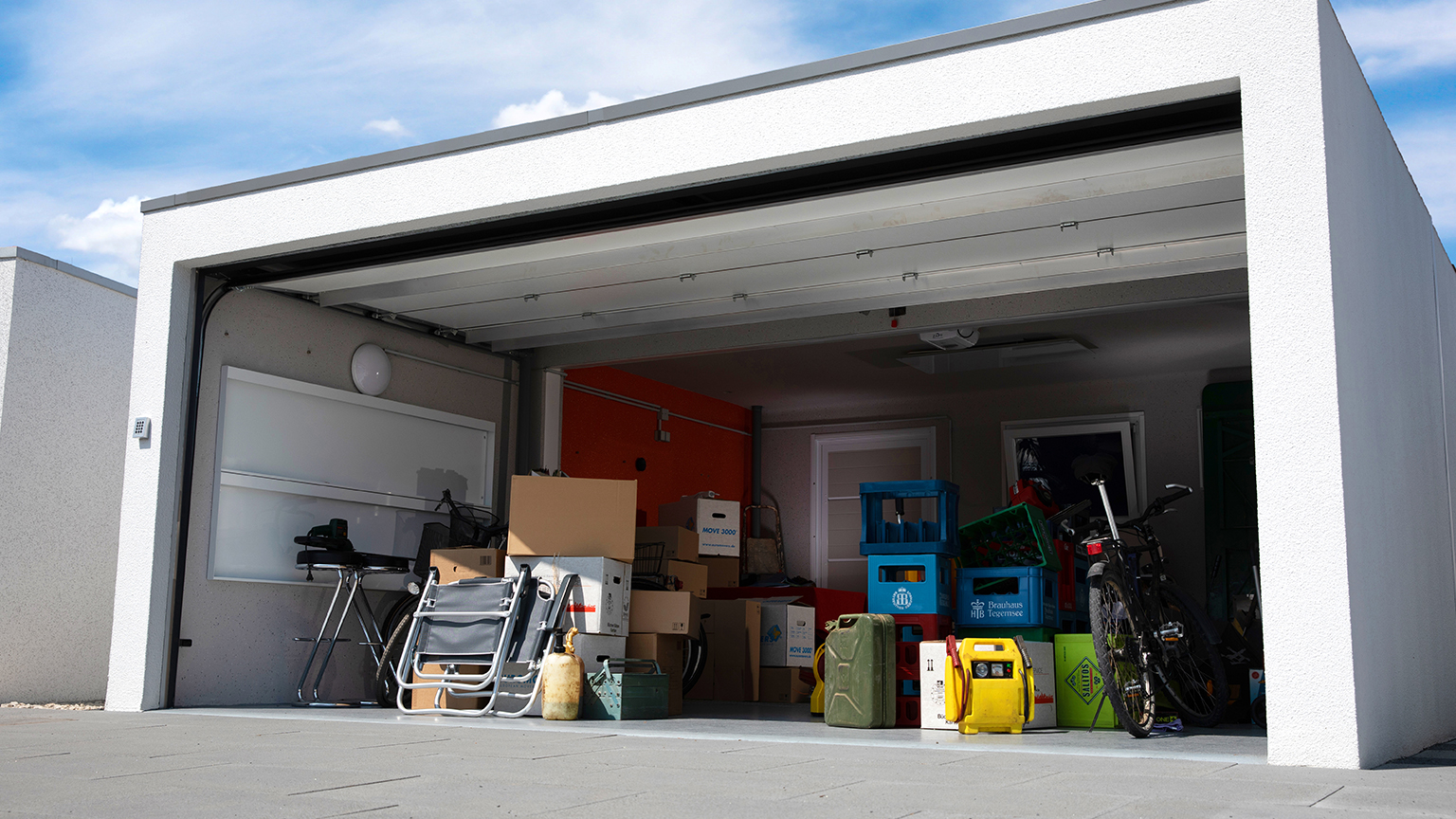 Garage mit geöffnetem Tor, voll mit Umzugskartons, Getränkekisten, Klappstühlen und Fahrrädern – vielseitige Nutzung als Lagerraum.