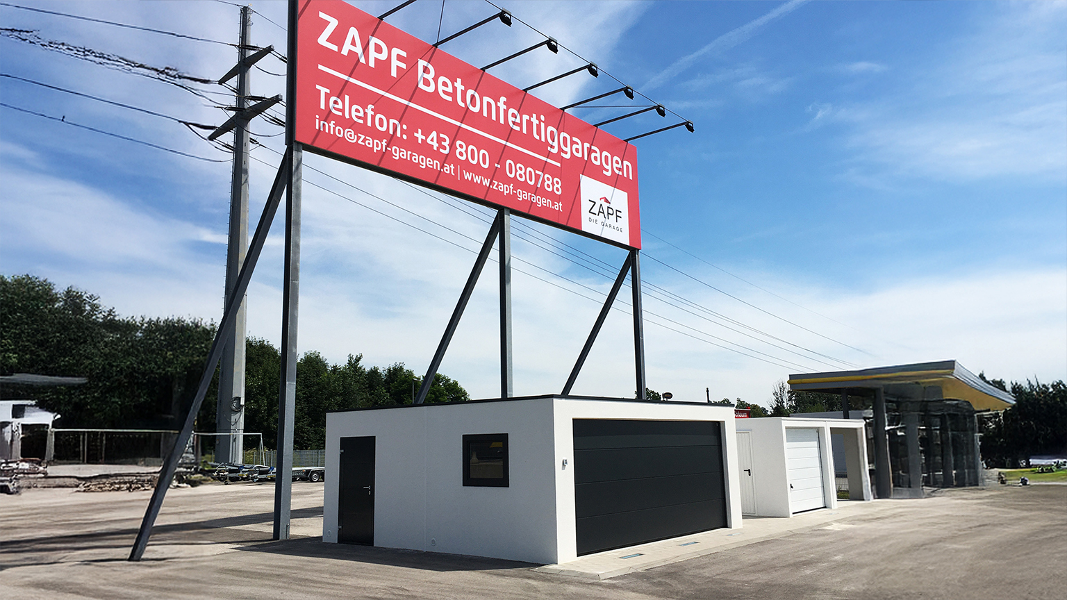 Musterstellplatz mit verschiedenen Betonfertiggaragen unter großem ZAPF Werbeschild auf einem Außengelände.