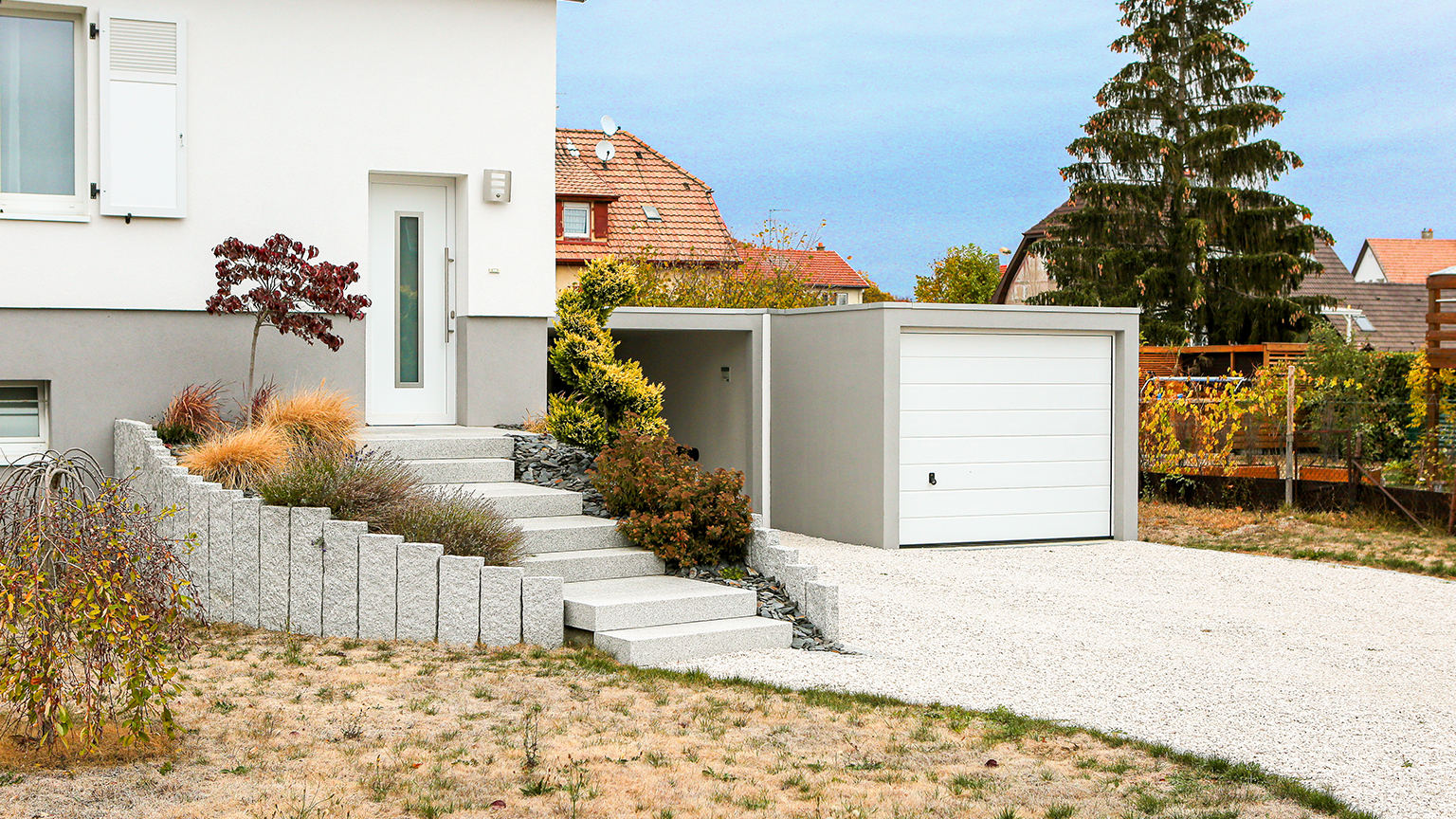 Weiße Garage mit grauem Rahmen neben moderner Hauseingangstreppe in Hanglage
