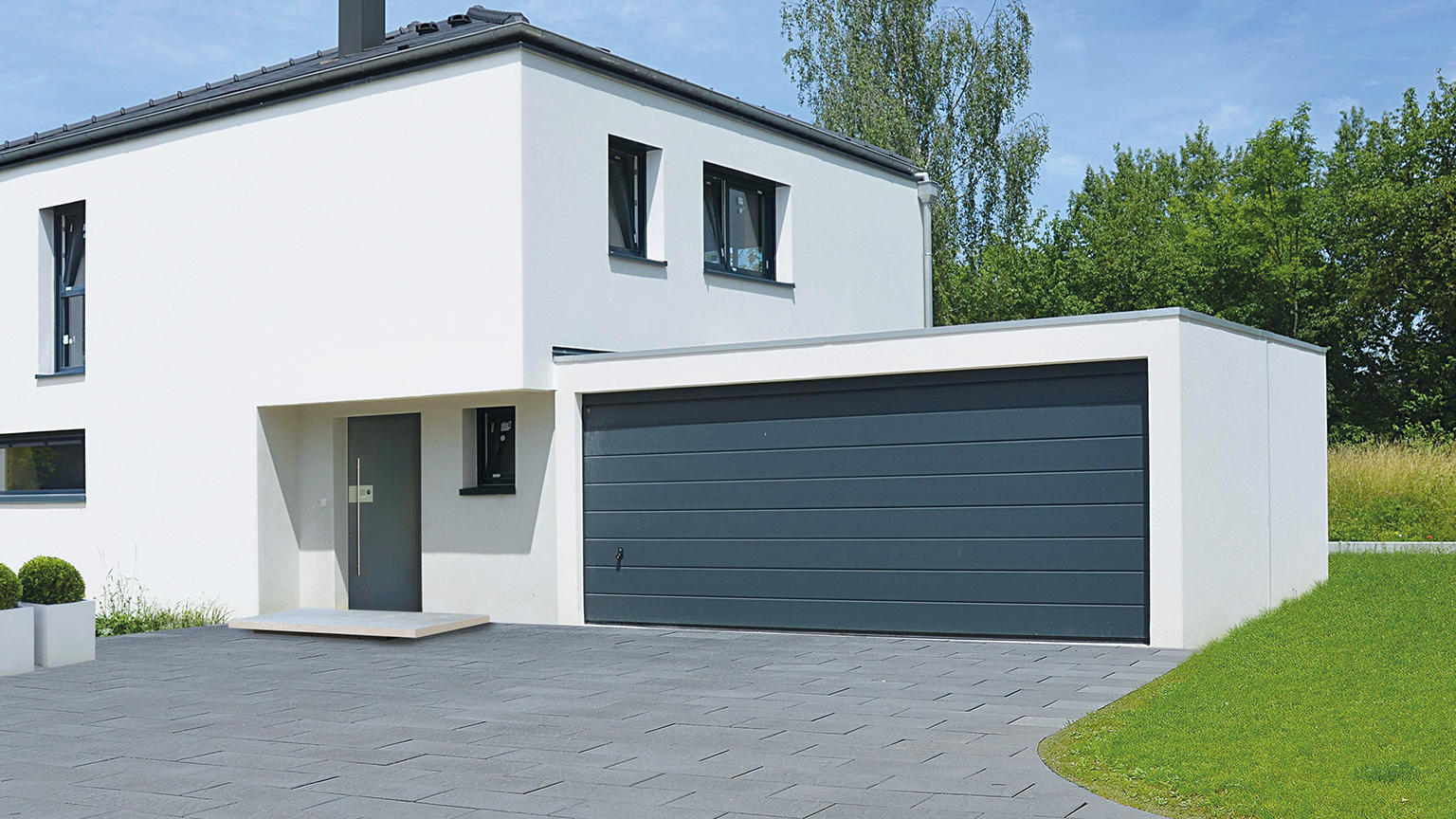 Moderne weiße Fertiggarage mit dunkelgrauem Sektionaltor an einem Einfamilienhaus