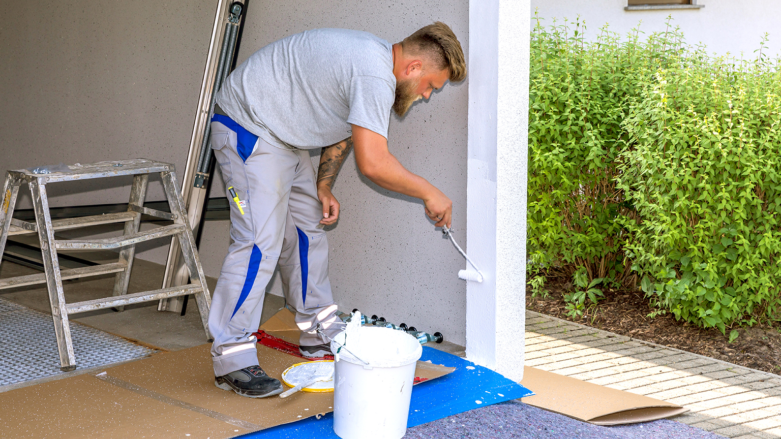 Handwerker streicht die Innenwand einer Fertiggarage mit weißer Farbe