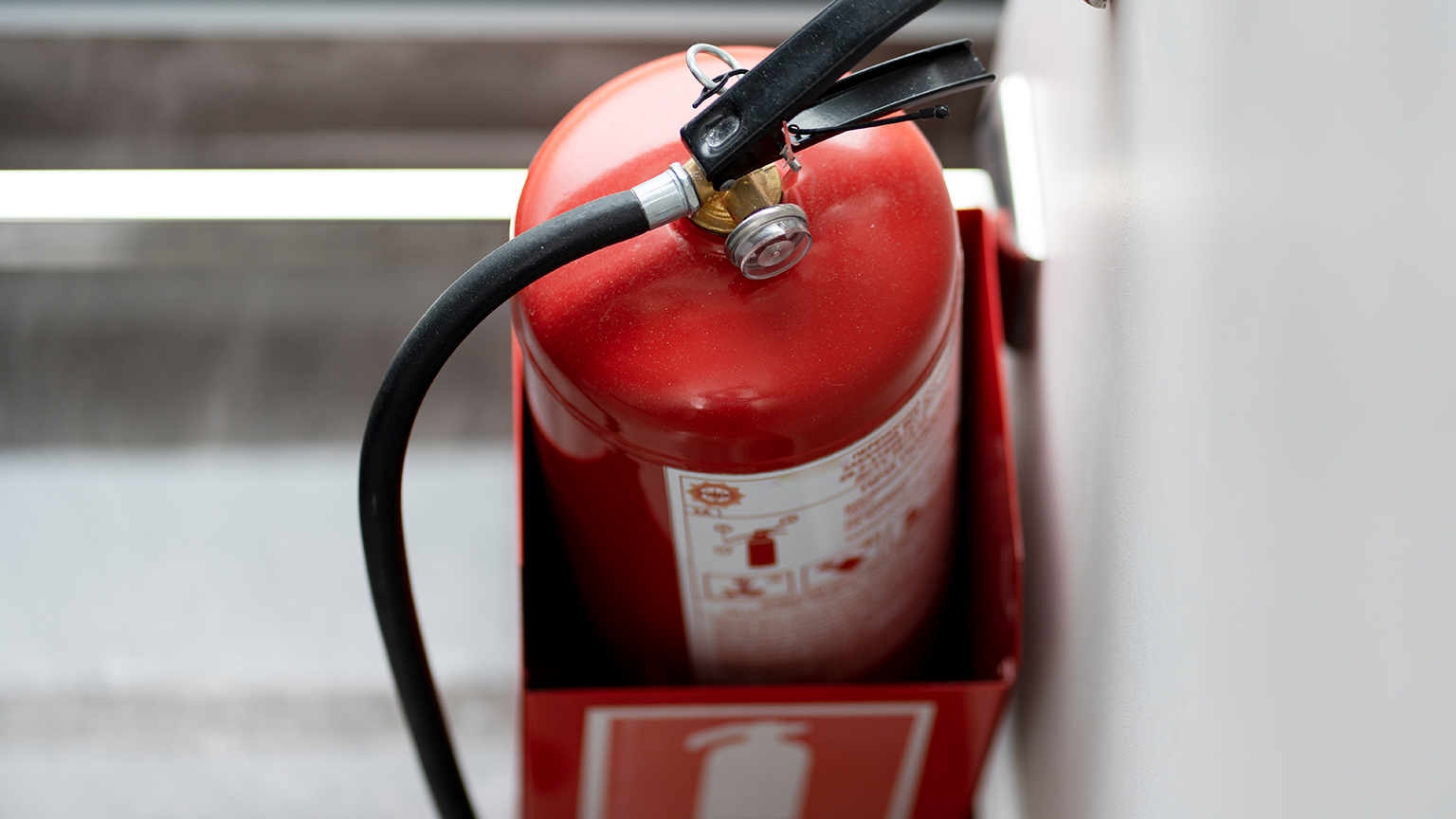 Roter Feuerlöscher in Wandhalterung aus Metall, fotografiert aus der Vogelperspektive.