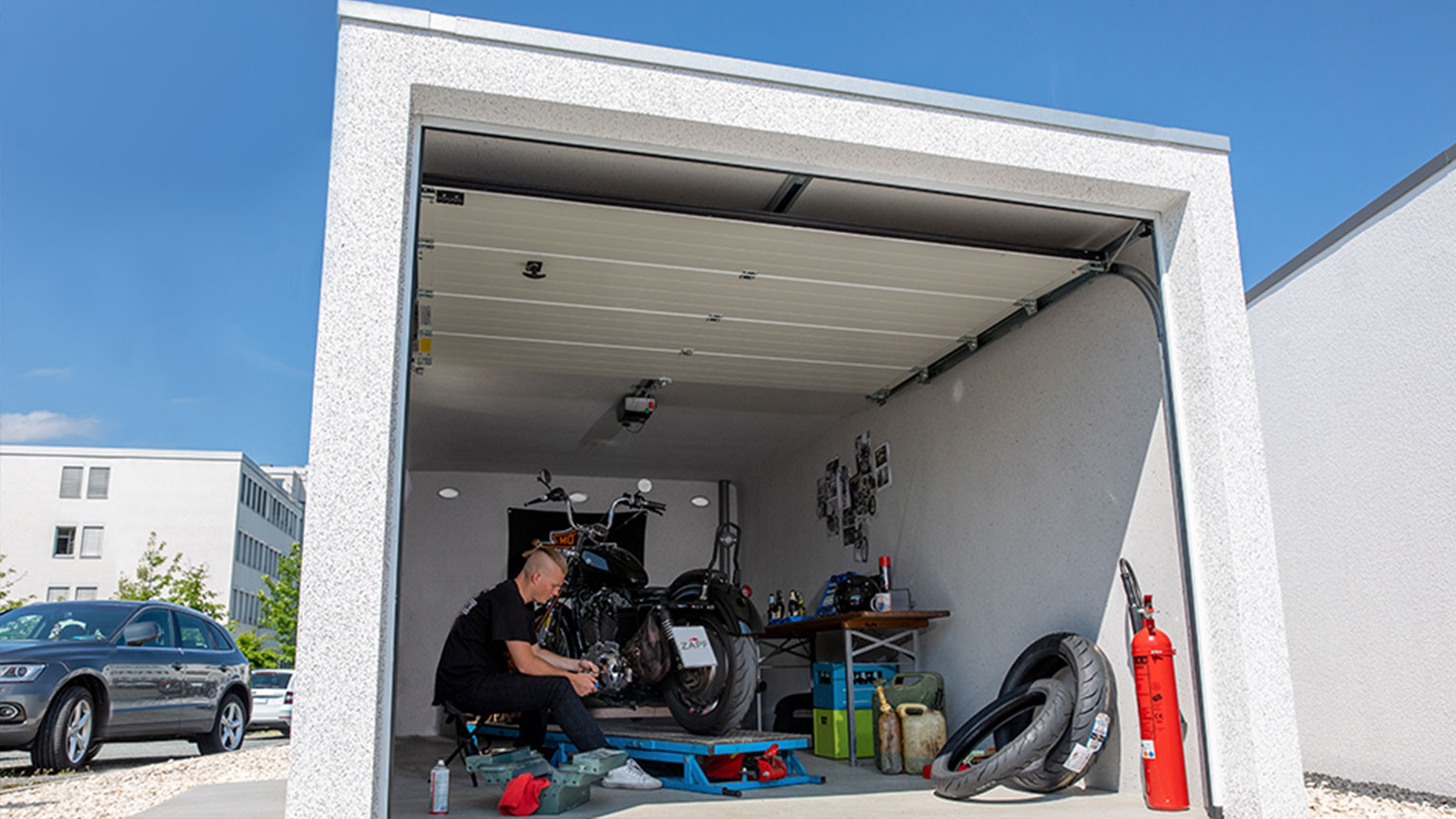 Person arbeitet an einem Motorrad in einer modernen Garage mit geöffnetem Garagentor und Werkzeugen.