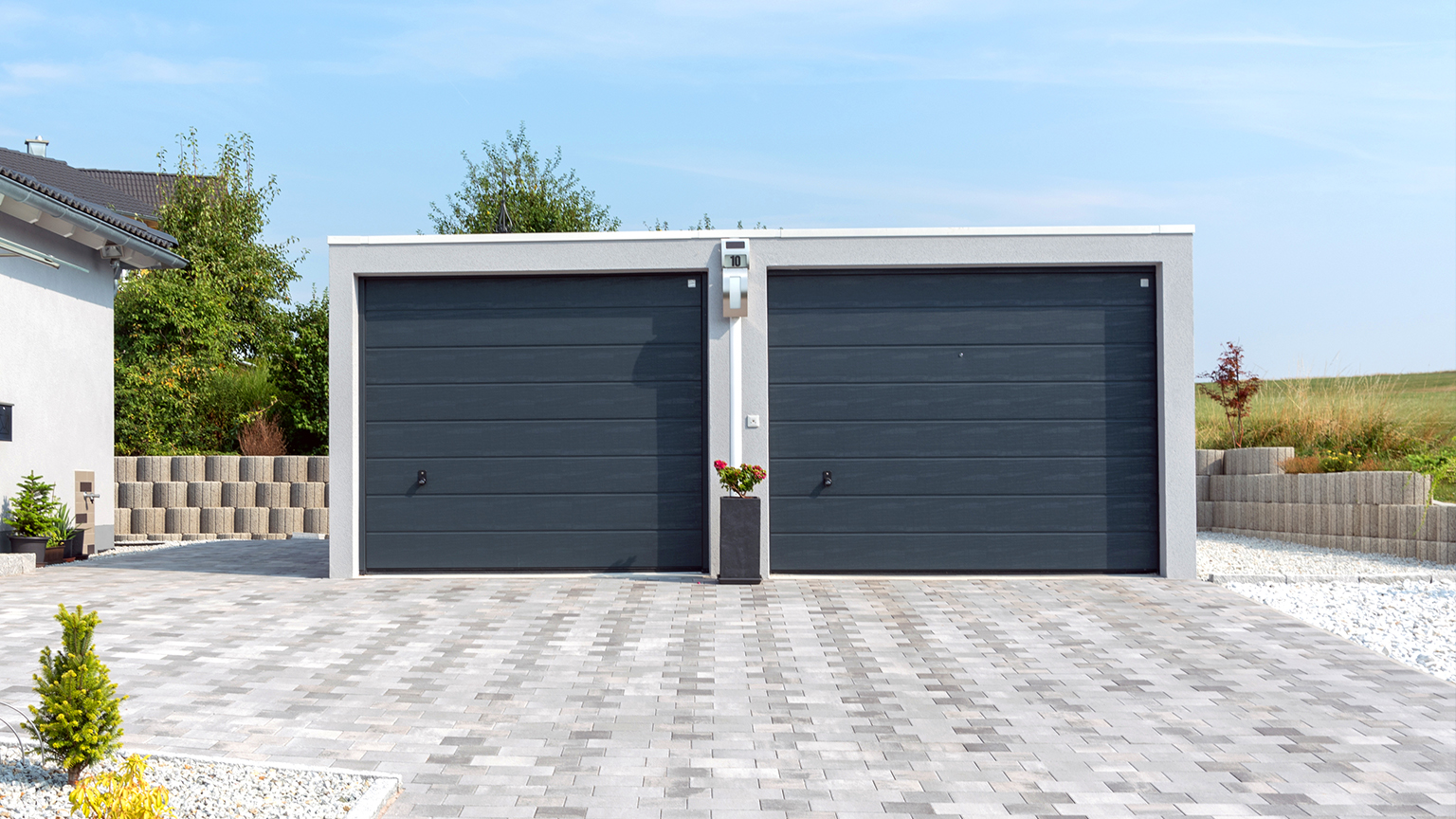 Doppelgarage mit anthrazitfarbenen Sektionaltoren und grauer Pflastersteinauffahrt in moderner Wohnsiedlung.