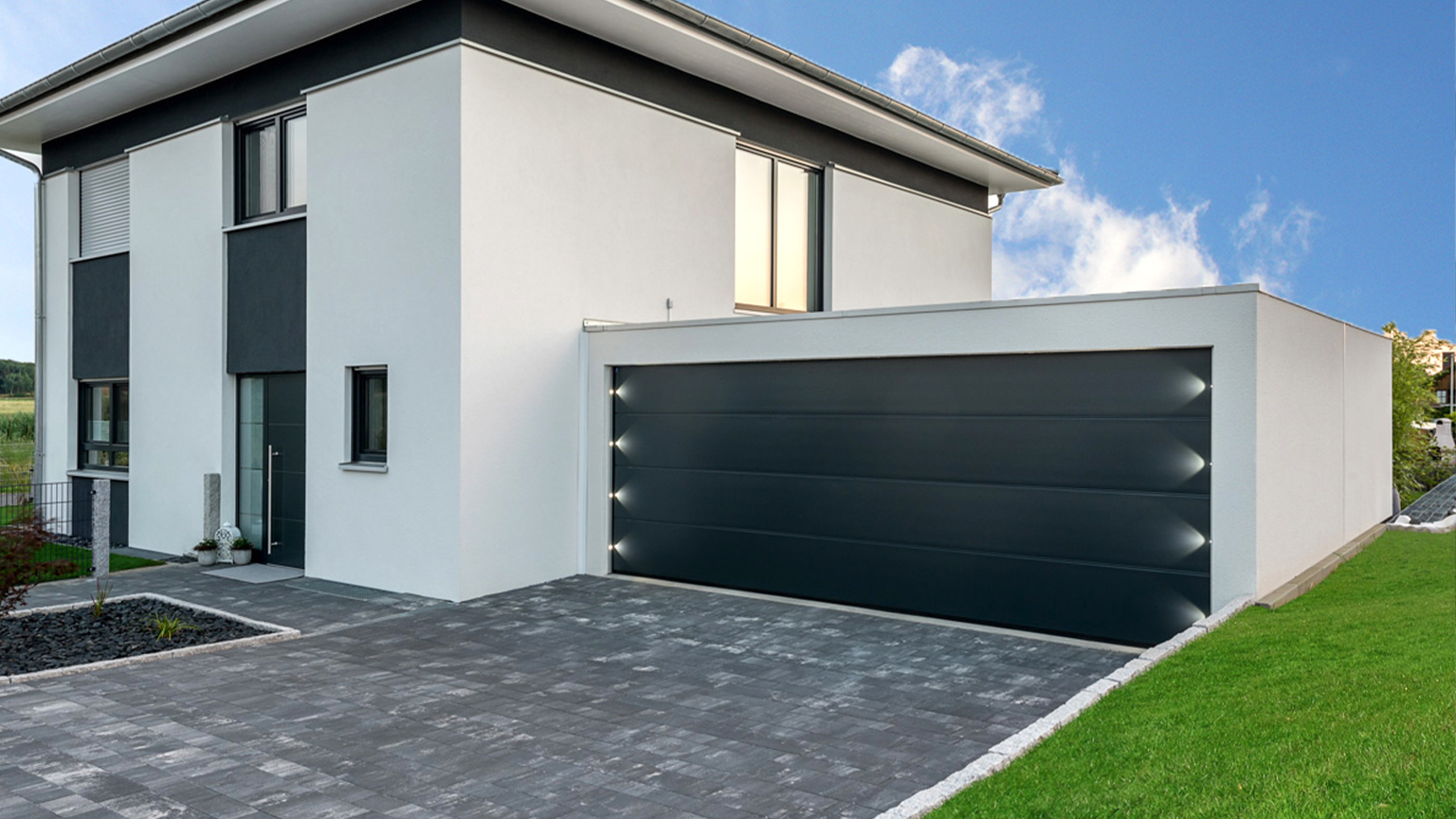 Design-Doppelgarage mit beleuchtetem schwarzem Sektionaltor direkt am modernen Einfamilienhaus.
