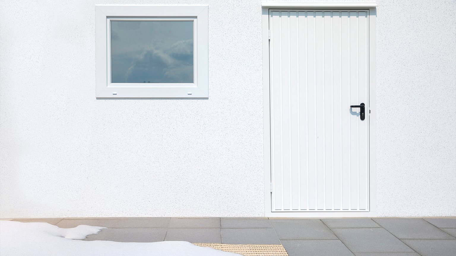 Seitentür und Fenster einer weißen Garage mit Schneeresten auf dem Boden