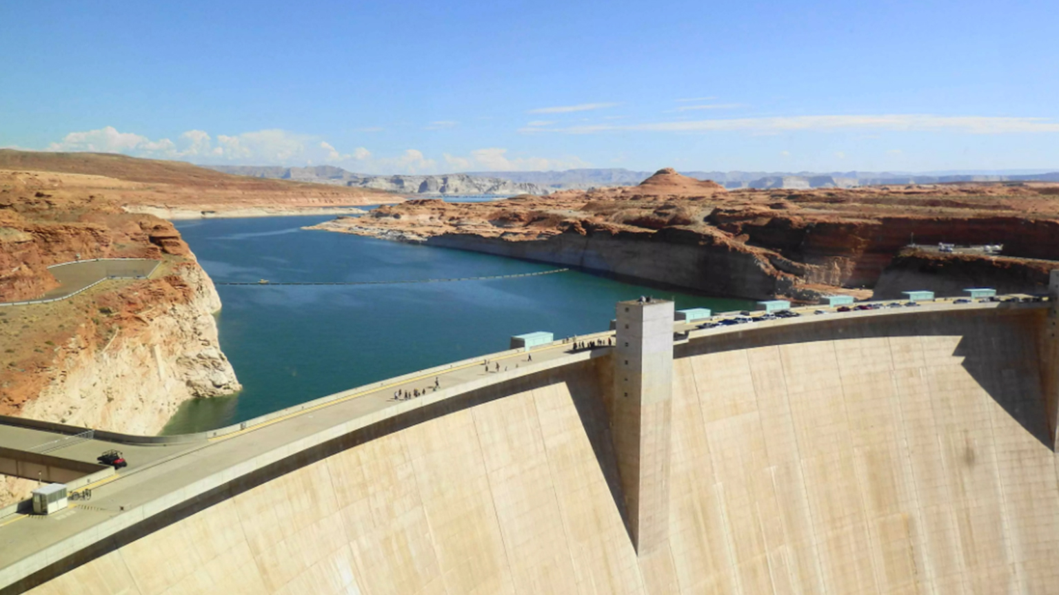 Blick auf den Glen Canyon Dam mit dem Colorado River und der umliegenden roten Felsenlandschaft bei klarem Himmel.