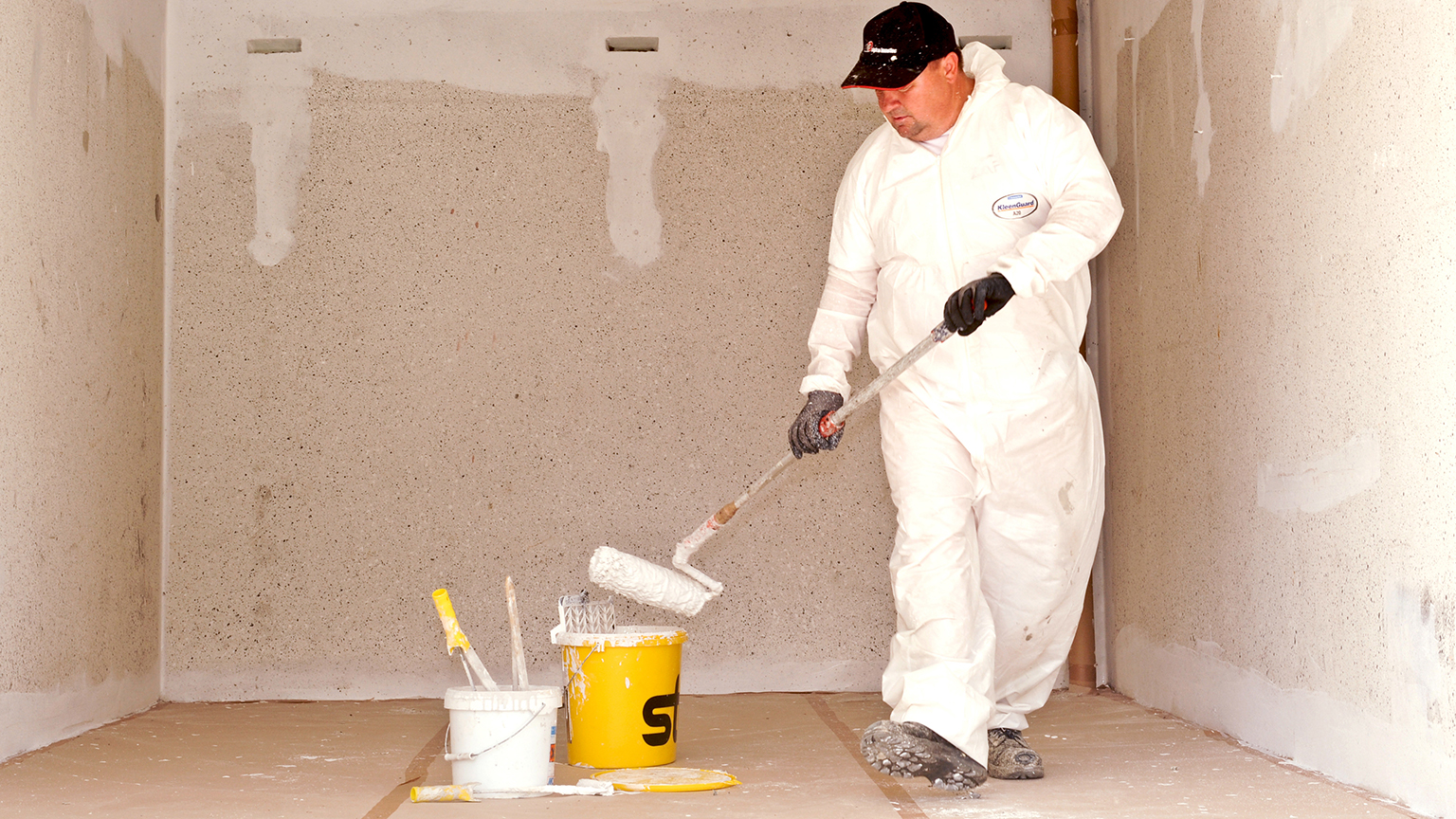 zapf_blog_beitragstitel_in_die_jahre Maler im weißen Overall streicht Garageninnenwand mit weißer Farbe und Farbrolle.