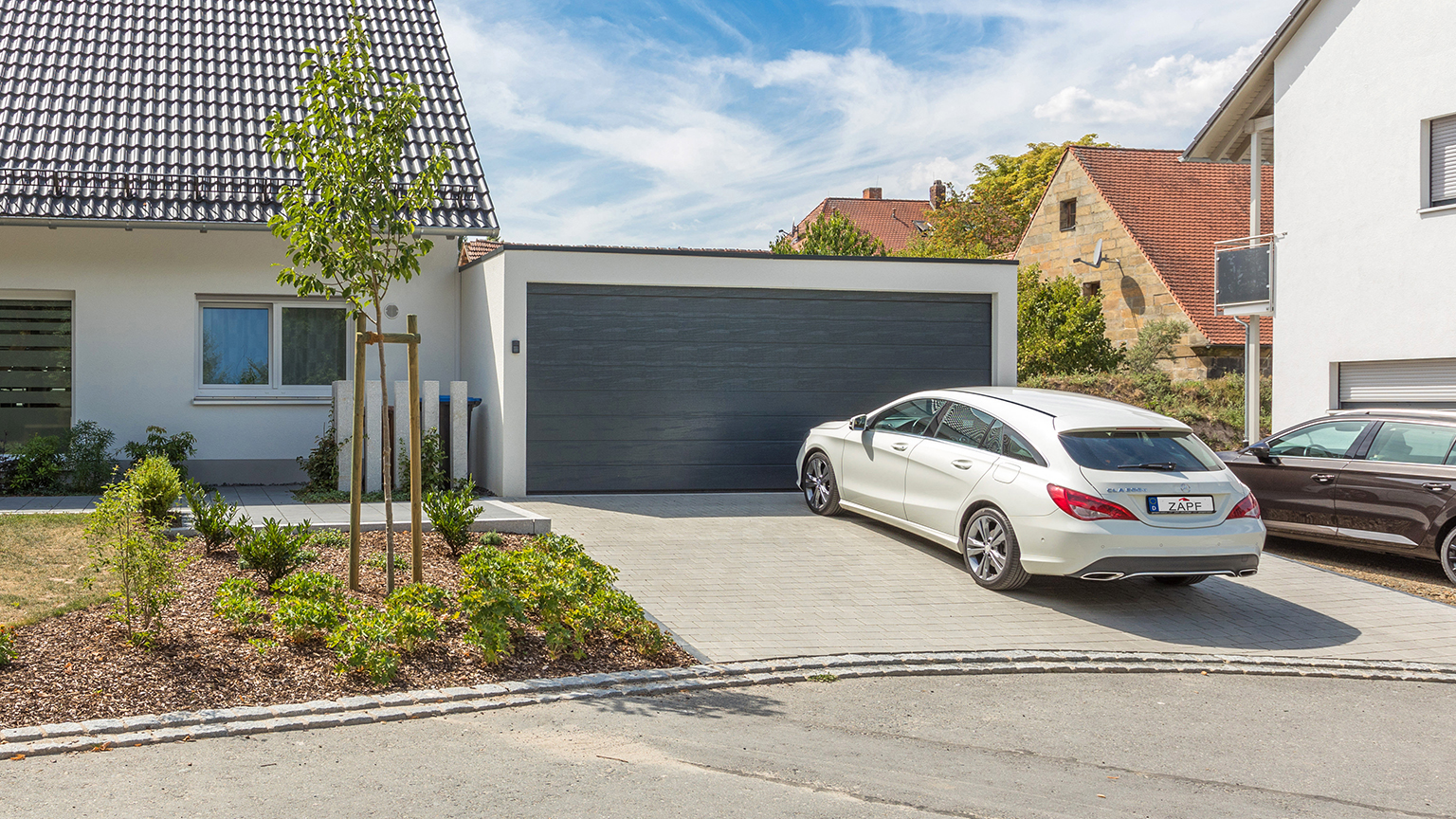 Moderne Doppelgarage mit dunklem Tor vor Einfamilienhaus, Mercedes vor der Einfahrt geparkt.
