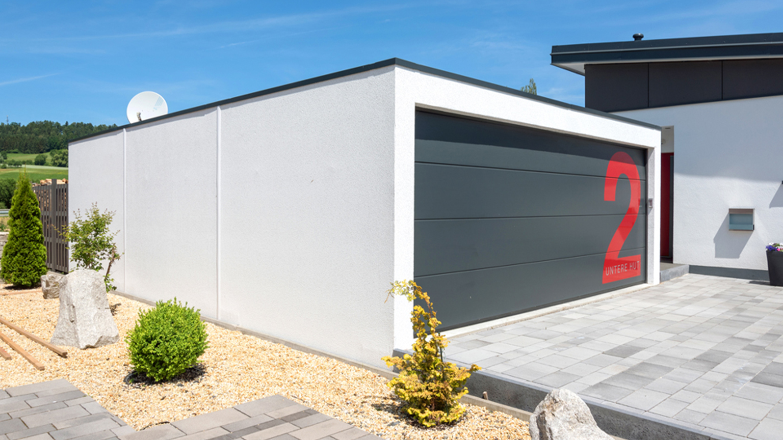 Moderne Fertiggarage mit grauem Tor und roter Hausnummer im Vorgarten