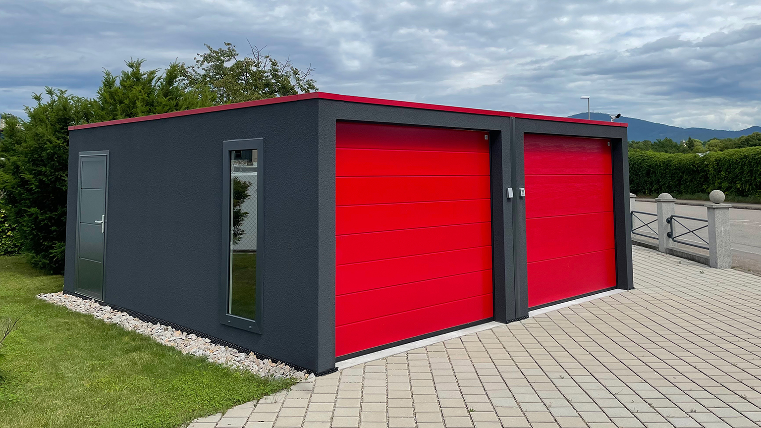 Zweifarbige Designgarage mit schwarzer Fassade und roten Sektionaltoren auf gepflasterter Fläche.