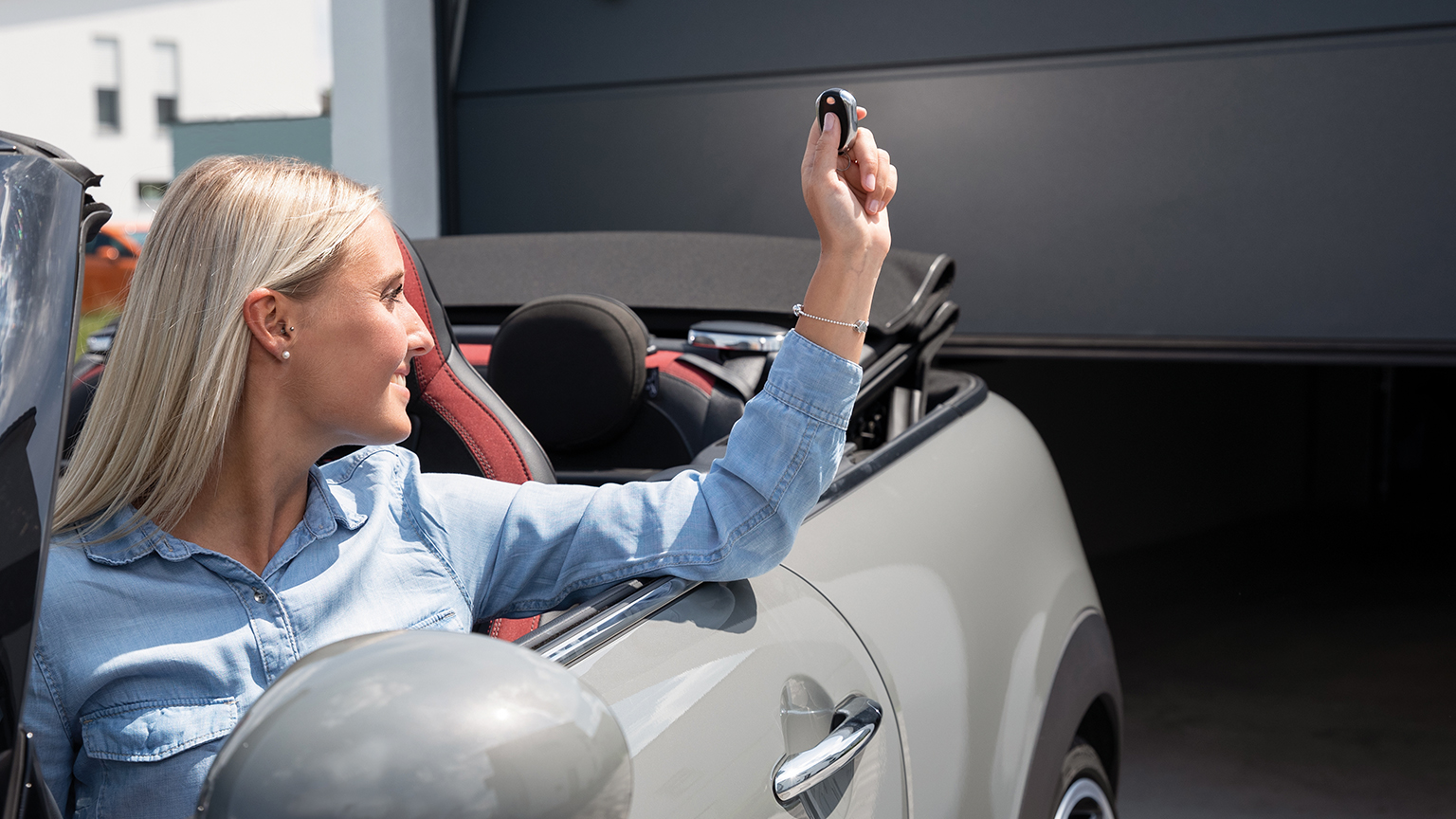 Frau im Cabrio öffnet per Funkfernbedienung das Garagentor aus dem Fahrzeug heraus.