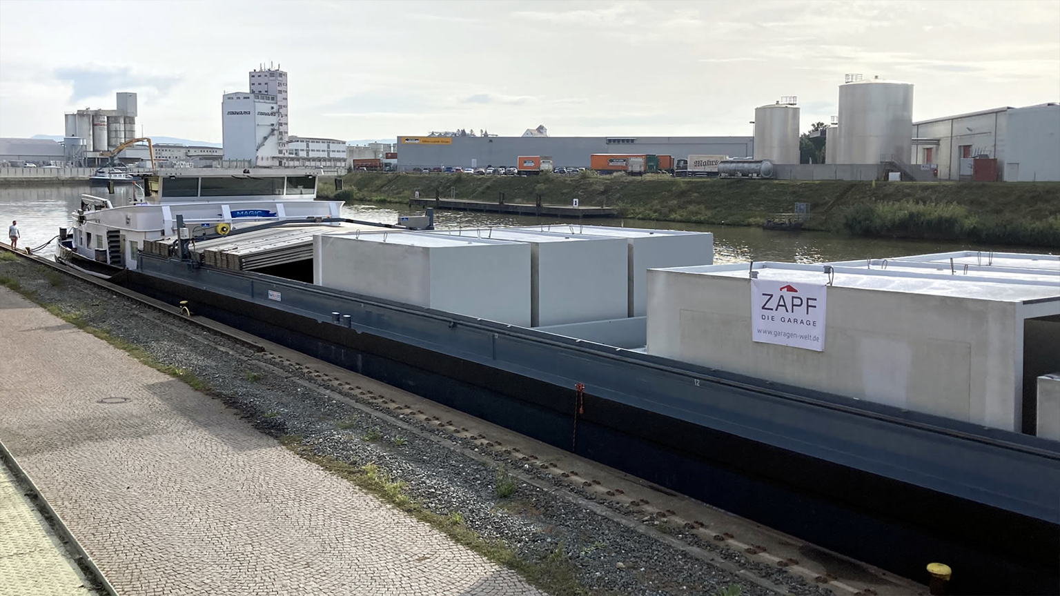 Mehrere Fertiggaragen auf einem Schiff das auf einem Kanal fährt.