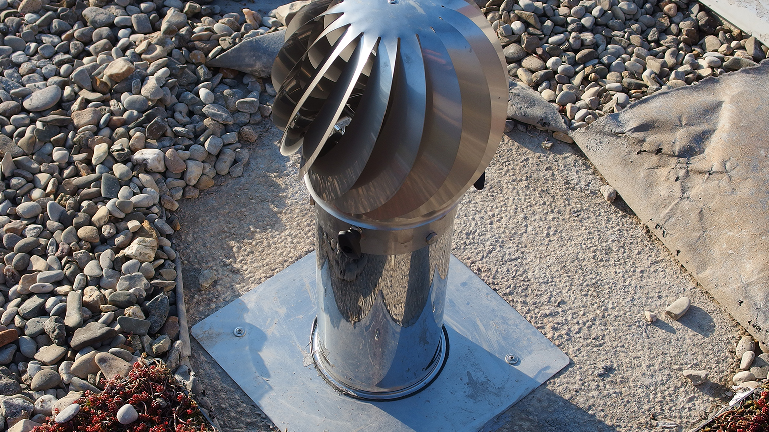 Rotierender Dachventilator aus Edelstahl auf extensiv begrüntem Flachdach mit Kiesfläche.