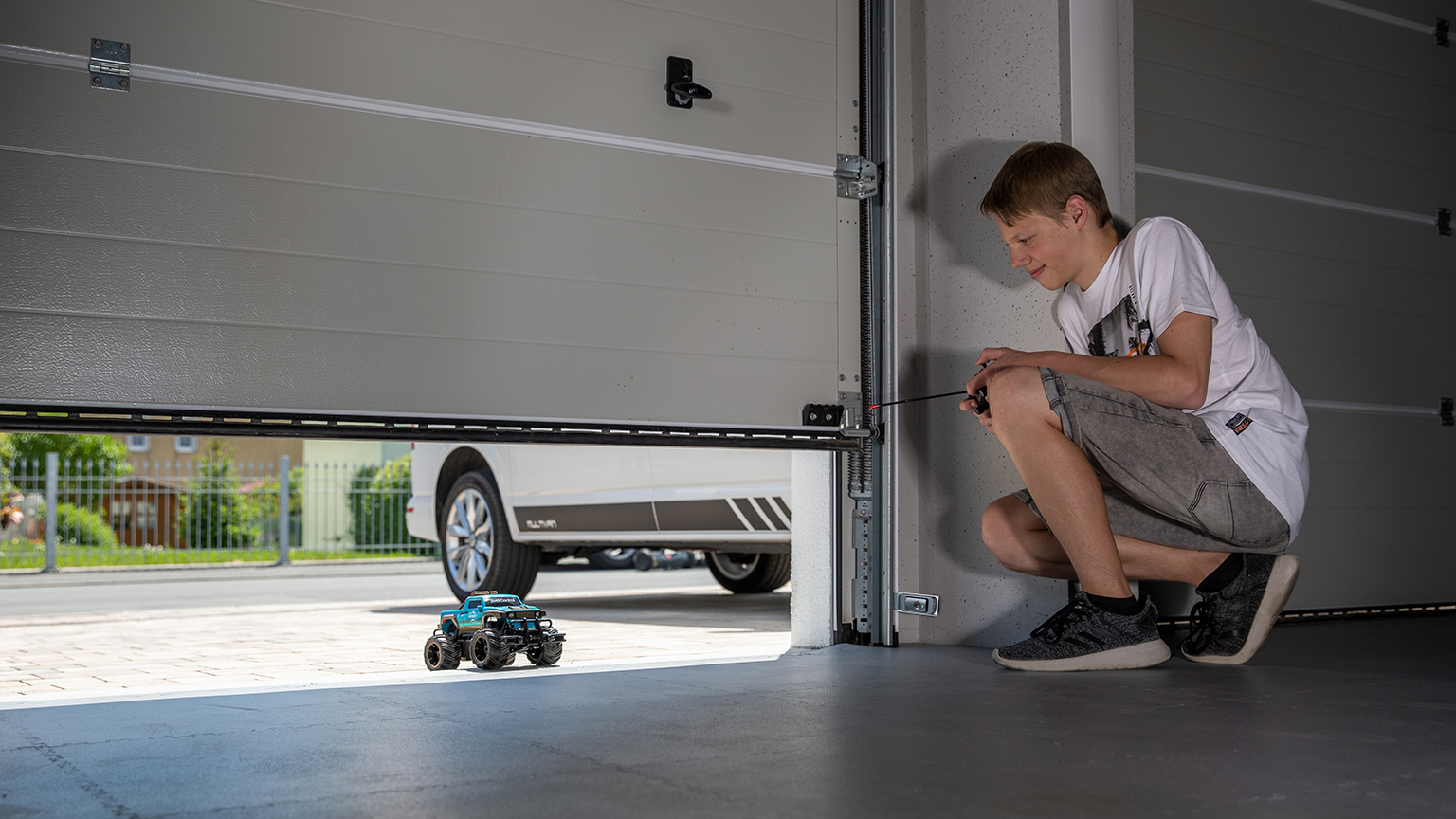 Junge spielt mit ferngesteuertem Auto in geöffneter Garage und nutzt dabei den unteren Türspalt als Ausfahrt.