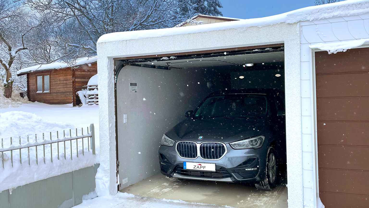 Ein geparktes Auto in einer verschneiten Garage im Winter mit schneebedecktem Dach.