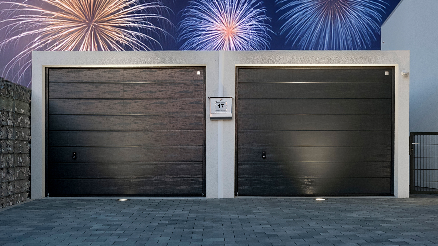 Doppelgarage mit stilvollem Design bei Nacht, darüber farbenfrohes Feuerwerk am Himmel.