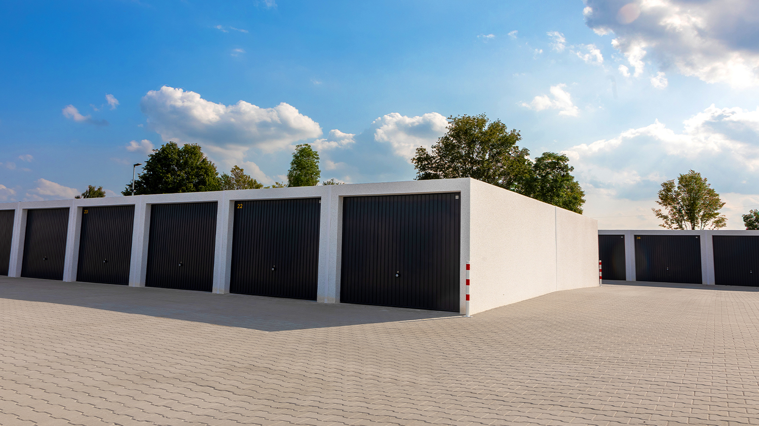 Reihengaragenanlage mit weißen Betonrahmen und schwarzen Schwingtoren auf großem Areal.
