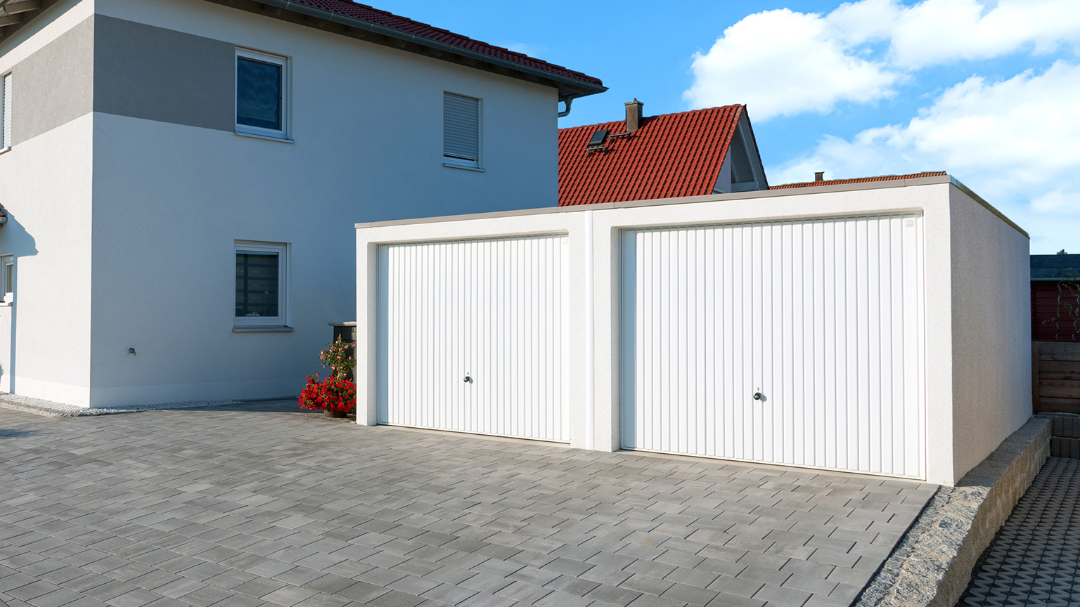 zapf_blog_beitragstitel_tipp Doppelgarage mit weißem Schwingtor neben modernem Wohnhaus auf gepflasterter Einfahrt.