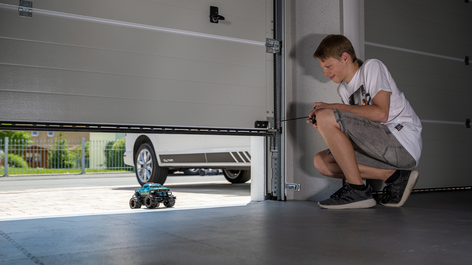 Junge spielt mit ferngesteuertem Auto vor halb geöffnetem Garagentor mit eingebautem Sicherheitssensor.