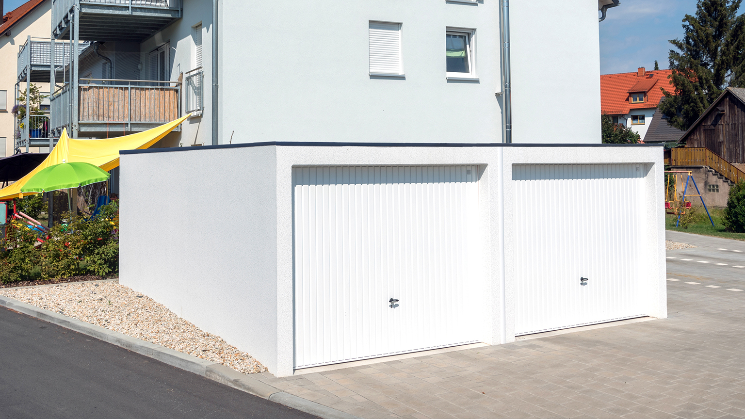 Doppelgarage mit weißen Schwingtoren vor einem Mehrfamilienhaus in städtischer Wohngegend