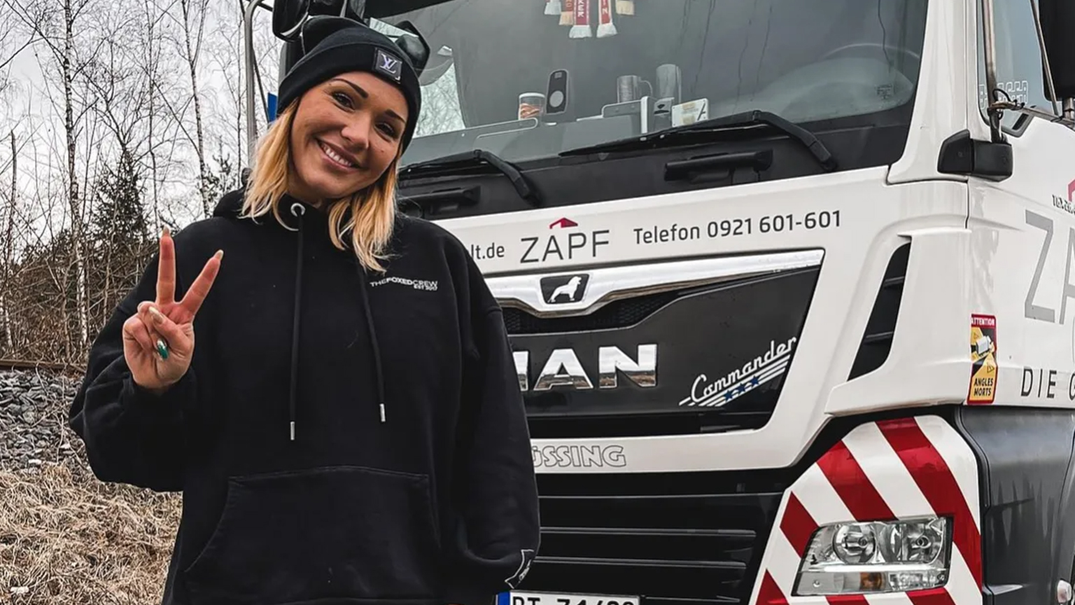 Lächelnde Frau in schwarzem Hoodie posiert vor ZAPF LKW mit Victory-Zeichen – Firmenlogo und Telefonnummer sichtbar.