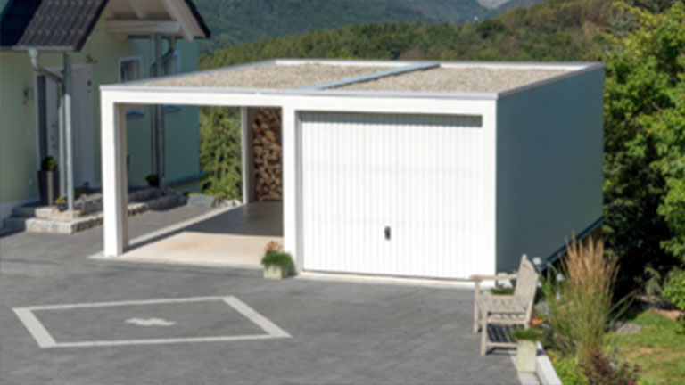 Carport à toit plat avec local à outils intégré et deux places de stationnement ouvertes dans un lotissement rural.