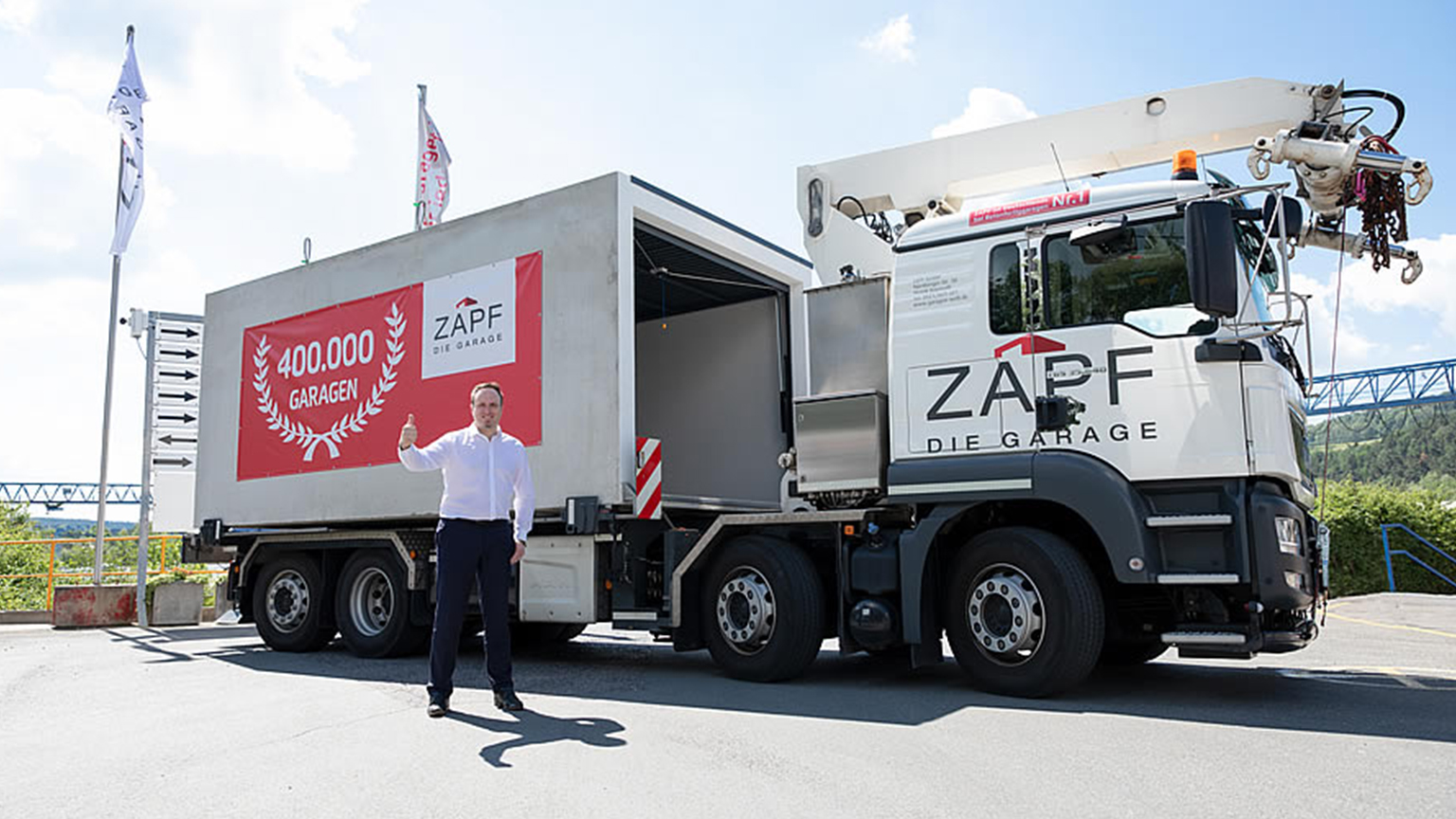 ZAPF Lkw mit transportfertiger Garage und Banner „400.000 Garagen“, daneben ein Mann mit Daumen hoch.