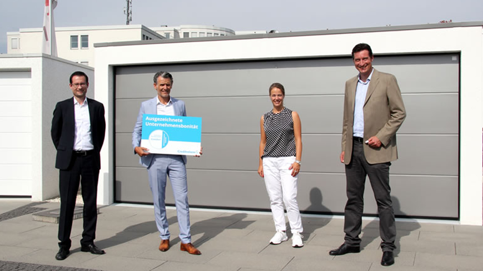 Vier Personen stehen vor moderner ZAPF Garage, eine davon hält ein Schild mit dem Bonitätszertifikat.