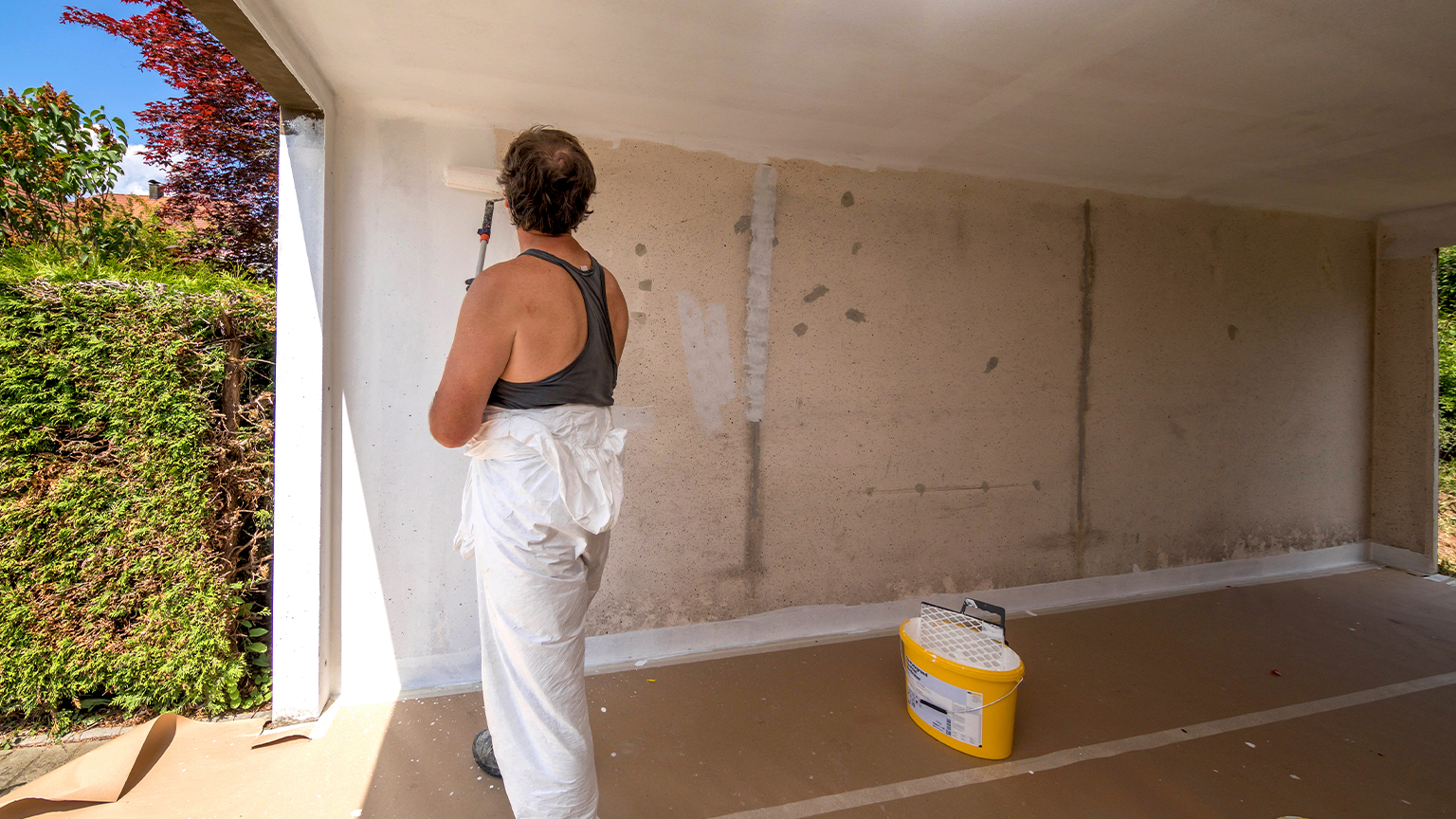 Handwerker streicht Innenwand einer Fertiggarage mit weißer Farbe.