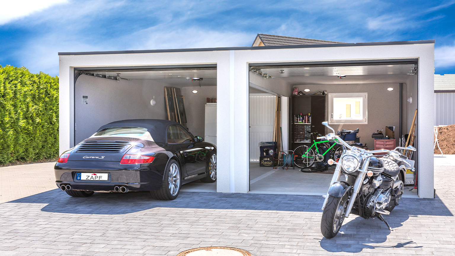 ZAPF Doppelgarage mit offenem Tor, darin ein schwarzer Porsche, Motorrad und Fahrräder vor der Garage.