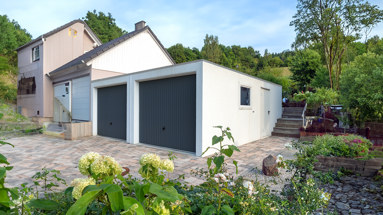 Doppelgarage mit dunkelgrauen Toren auf großzügigem Grundstück mit Garten und Hanglage.