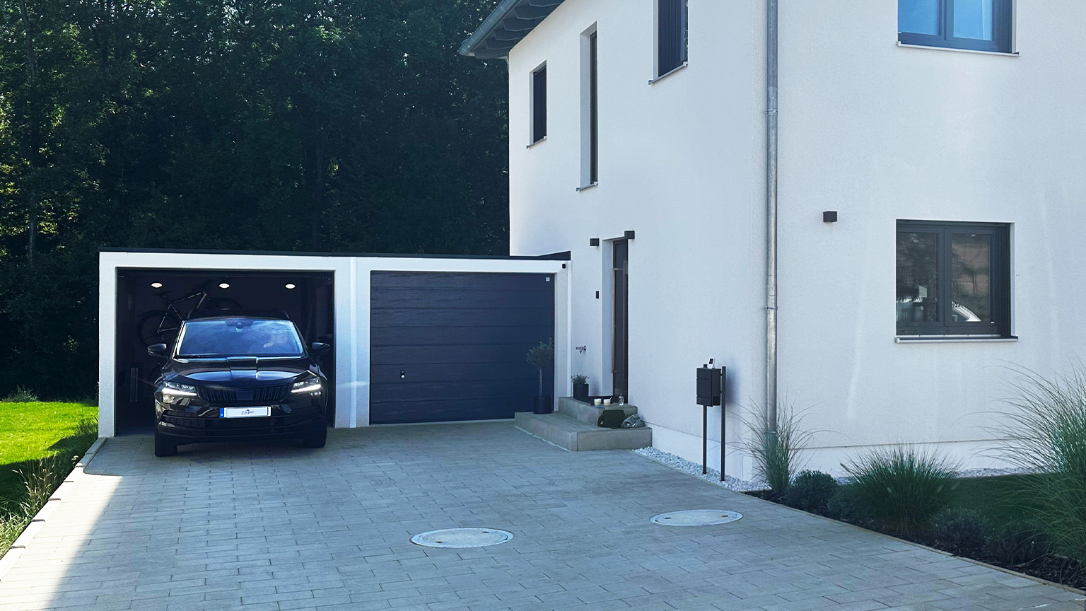 Moderne Doppelgarage mit offenem Stellplatz, geparktem SUV und angrenzendem Einfamilienhaus.