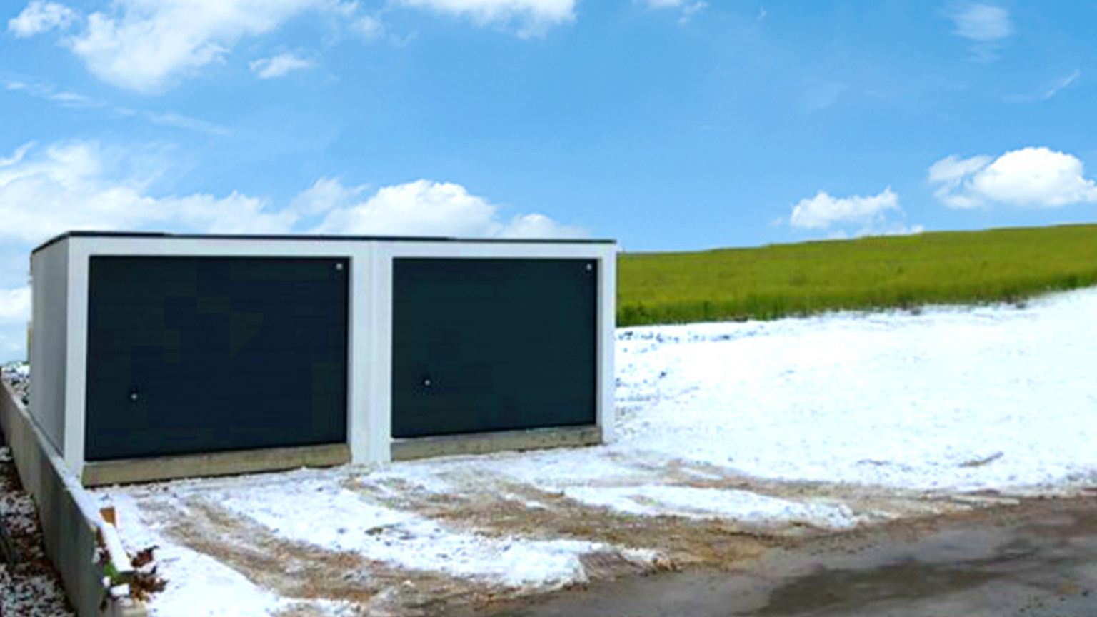 Doppelgarage mit dunklen Toren in verschneiter Landschaft am Rand eines offenen Feldes.