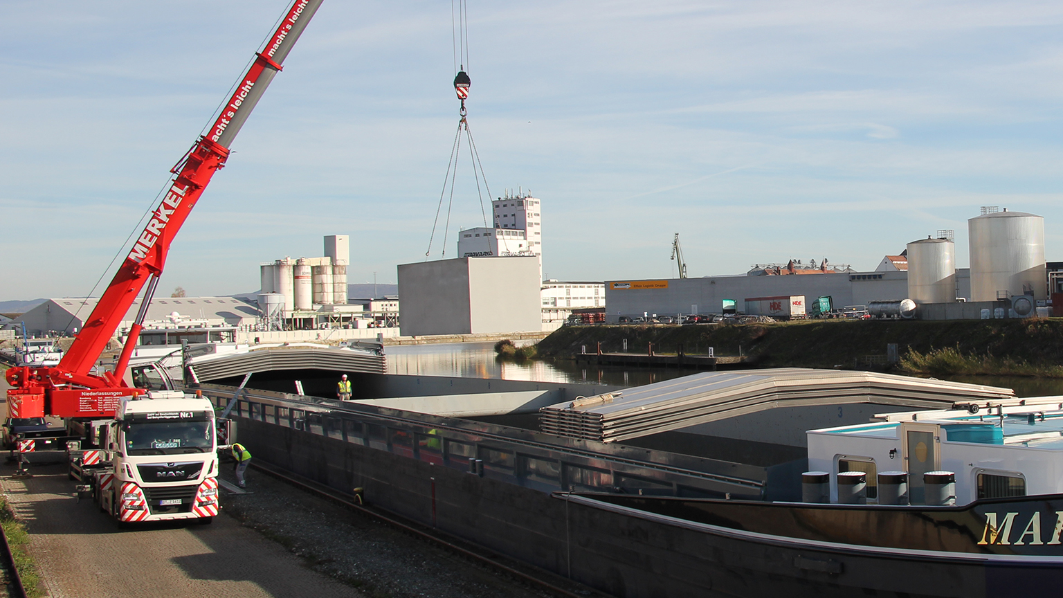 Schwerlastkran verlädt Fertiggaragenmodul von ZAPF auf Binnenschiff im Industriehafen.