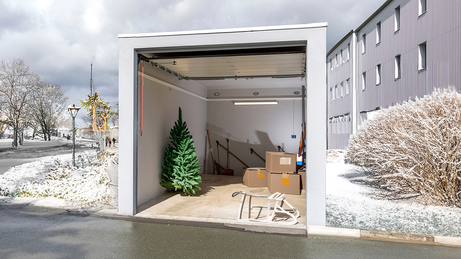 Geöffnete Garage im Winter mit künstlichem Tannenbaum, Kartons, Schlitten und Schneeschiebern.