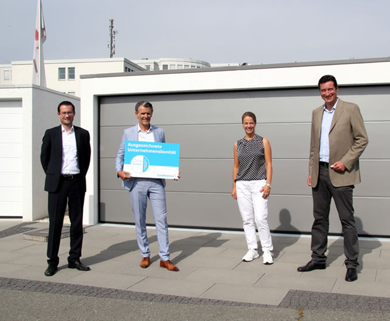 Group photo with four people in front of a gray prefabricated garage, presentation of the CrefoZert certificate.