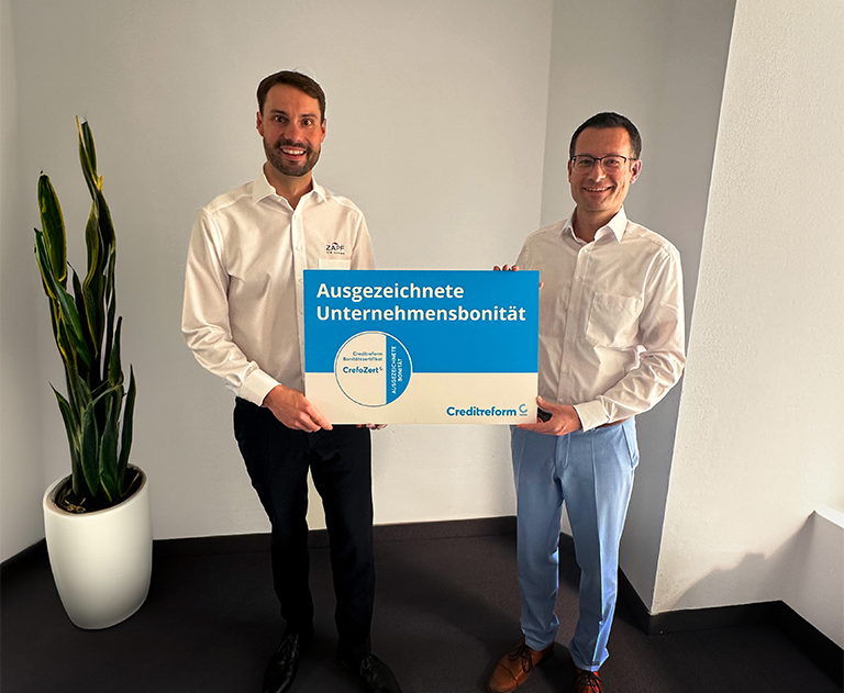 Zwei Männer in Businesskleidung halten Auszeichnungstafel „Ausgezeichnete Unternehmensbonität“ von Creditreform.