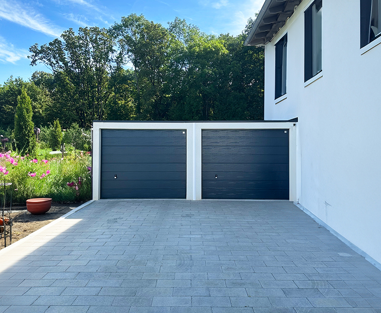 Doppelgarage mit anthrazitfarbenen Sektionaltoren auf geräumiger Einfahrt neben Gartenbereich.