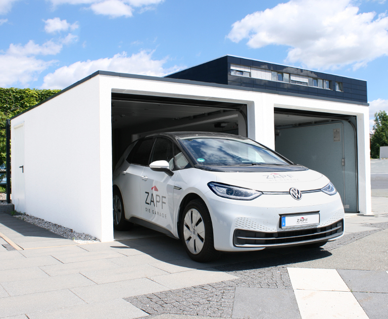 White VW ID.3 with ZAPF branding drives out of a modern prefabricated garage with two gates on a paved area.