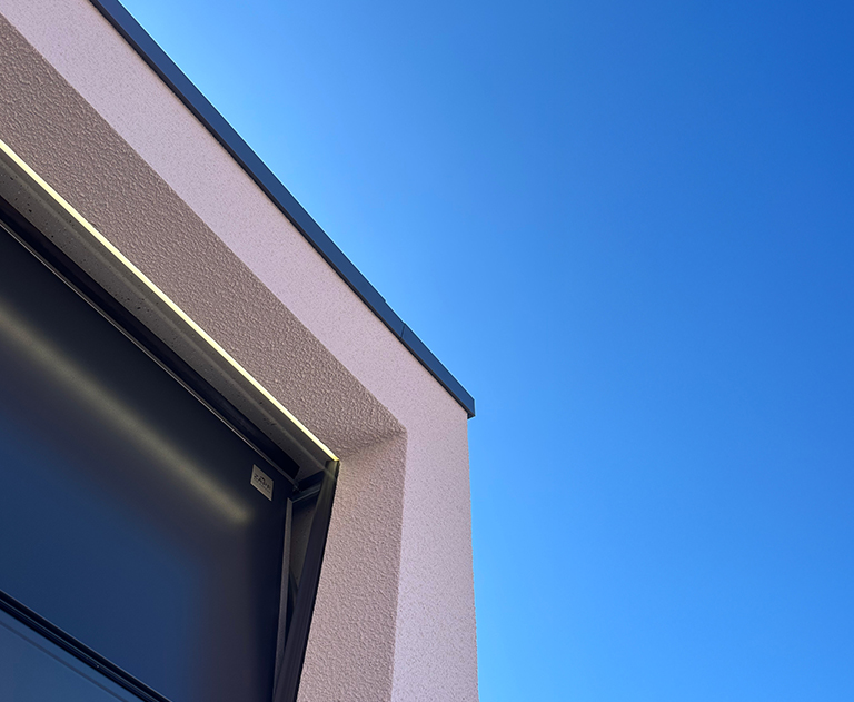 Oblique view of modern prefabricated garage with LED lighting and blue sky in the background.
