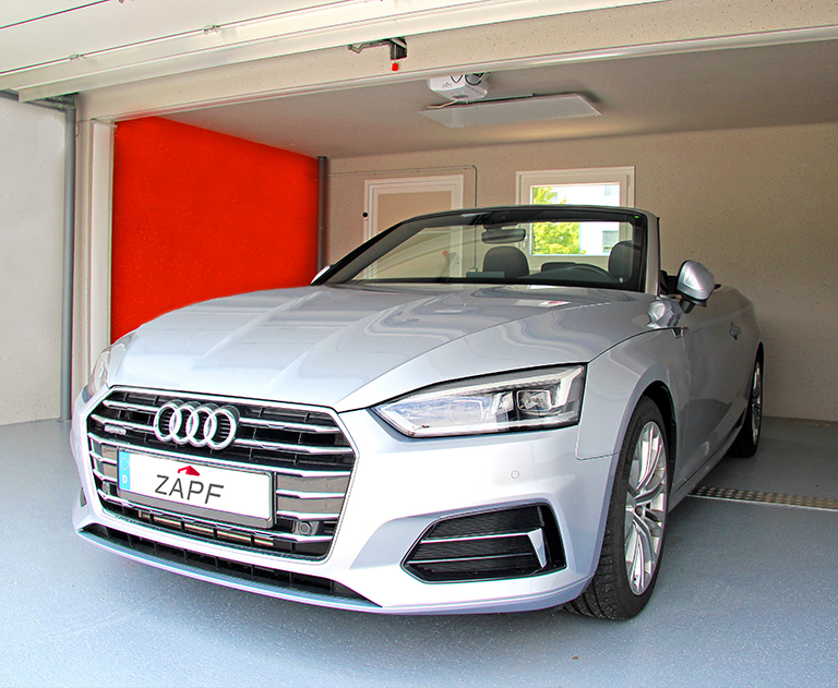 Silver Audi convertible with ZAPF license plates is parked in a high-quality garage with a red rear wall.