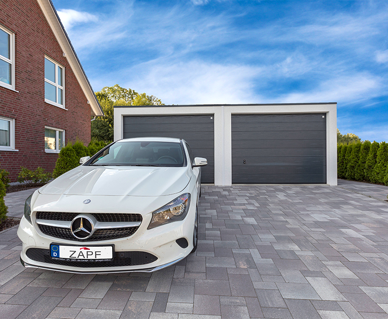 White Mercedes parked on a paved driveway in front of a ZAPF double garage with anthracite-colored doors.
