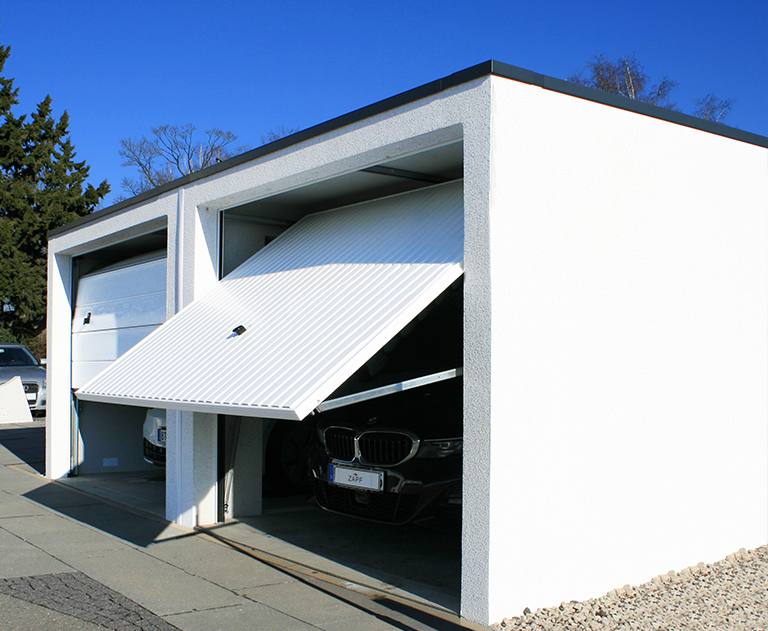 Garage préfabriqué blanc avec porte basculante entrouverte et BMW garée à l'intérieur.